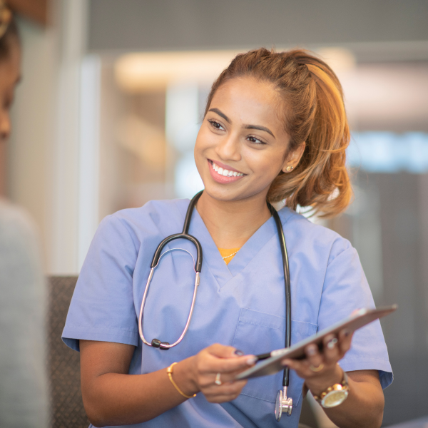Smiling female nurse practitioner or PA in blue scrubs holding a chart and consulting with a patient
